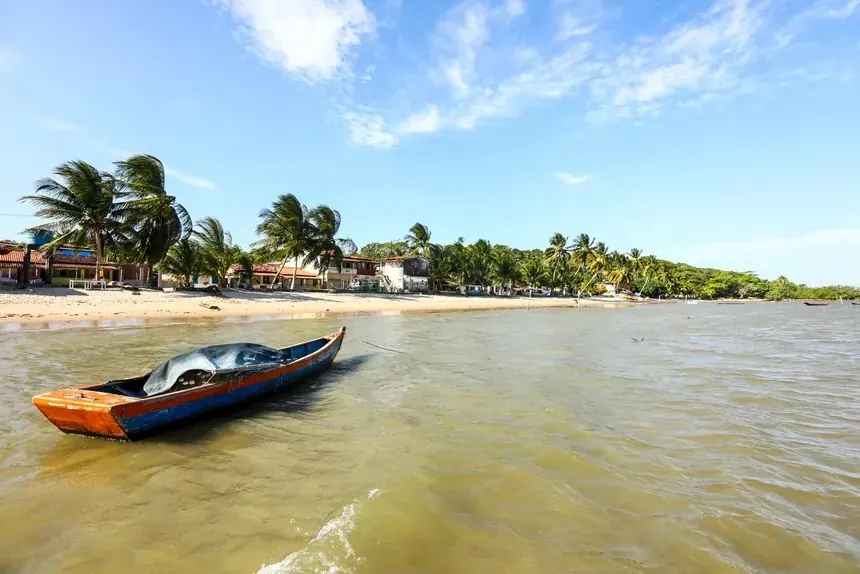 Canoa de madeira em água calma com coqueiros e vila ao fundo em Boipeba