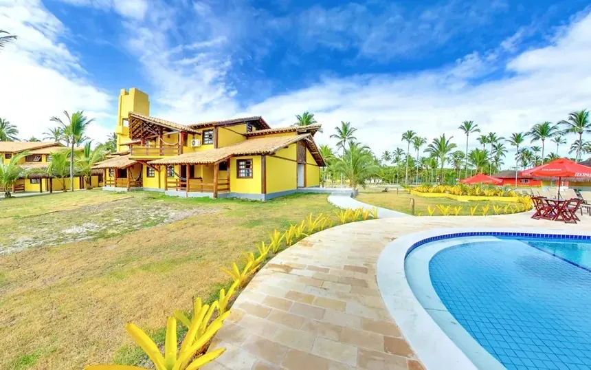 Hospedagem amarela com piscina, coqueiros e jardim tropical